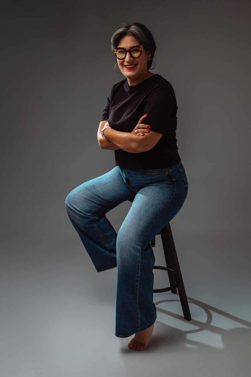 Laura sentada en un taburete del estudio, sonriendo con los brazos cruzados